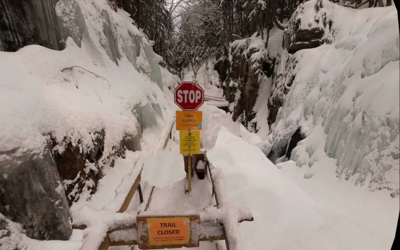 Image of a snow and ice covered bridge with a STOP sign and "Trail Closed" sign