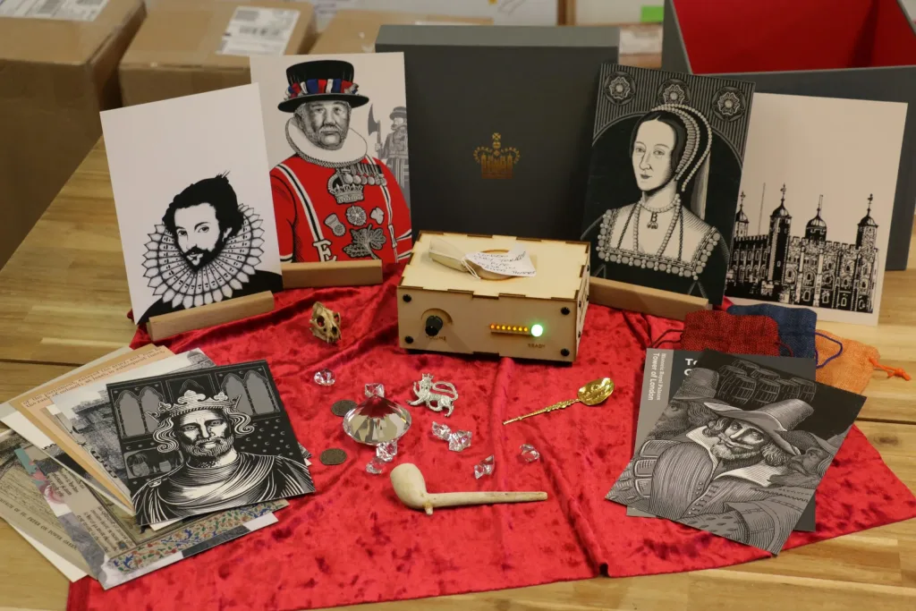 An tabletop with a wooden box with lights and a knob surrounded by various historical portraits and some artifacts.