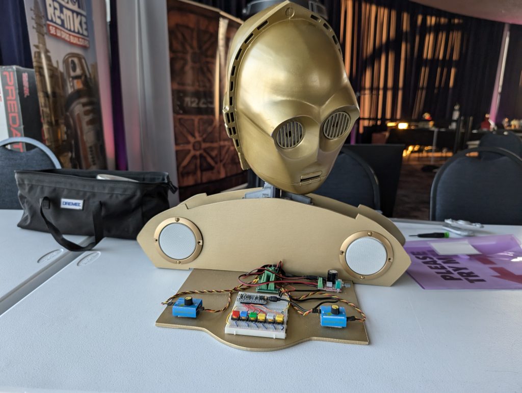 The head of C-3PO (from Star Wars) with speakers and some switchers sitting on a table.